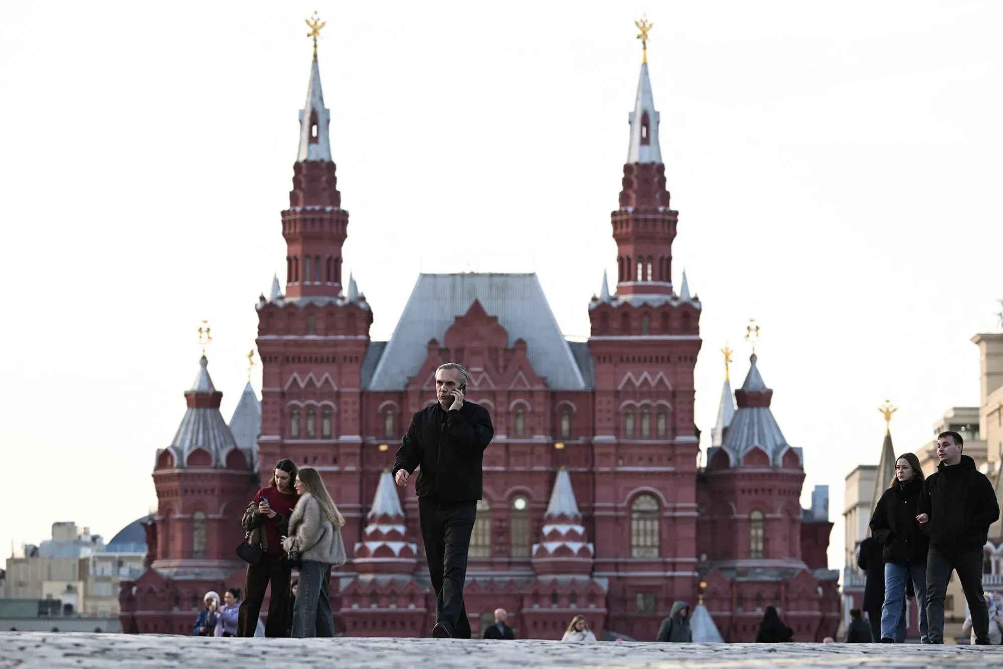 رجل يتحدث على الهاتف بينما يسير في ساحة حيوية بموسكو، مع خلفية لمبنى تاريخي مميز، يعكس تأثير انقطاع الإنترنت على الحياة اليومية.