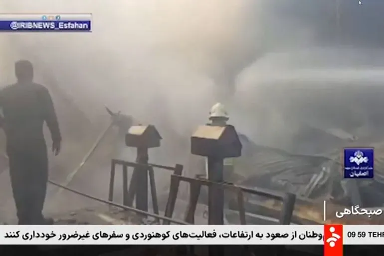 تحطم مروحية عسكرية في سوق للفاكهة بأصفهان، مع وجود رجال إطفاء يحاولون إخماد الحريق وسط الدخان الكثيف.