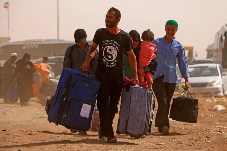 لاجئون أفغان يحملون حقائبهم على الحدود الإيرانية، مع تزايد المخاوف من الترحيل الجماعي وسط أزمة إنسانية.