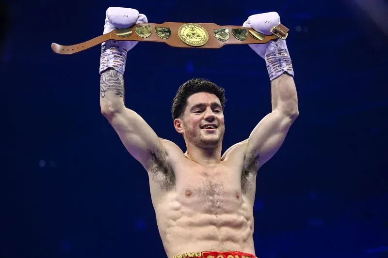 جون كوني، الملاكم الأيرلندي، يحتفل بفوزه بلقب وزن الريش الخارق، رافعًا الحزام في ساحة النزال، تعبيرًا عن فرحته.