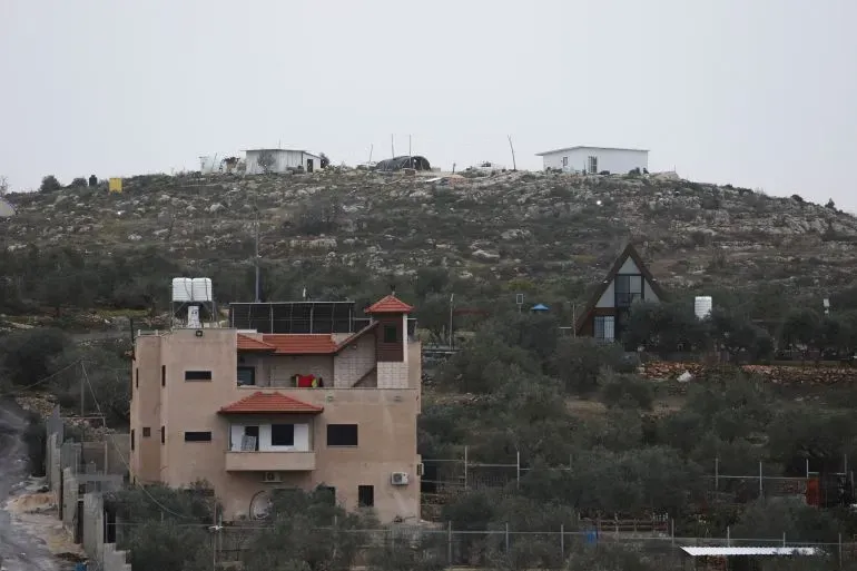 منازل تقع في منطقة جبلية بالضفة الغربية، تعكس التوترات حول الاستيطان الإسرائيلي وقرارات الحكومة بشأن تسجيل الأراضي كأملاك دولة.