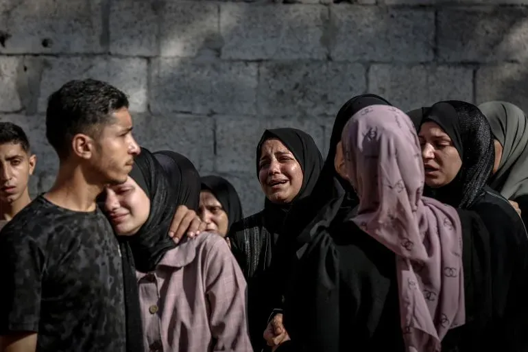 نساء وأطفال فلسطينيون يبكون بحزن في غزة بعد تصاعد العنف والتهجير، وسط دمار خلفته الغارات الجوية الإسرائيلية.