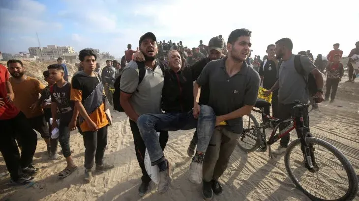 محتشدون في غزة يحملون شخصًا مصابًا بعد هجوم إسرائيلي، يعكس مشاهد المعاناة والبحث عن المساعدة amid ongoing humanitarian crisis.