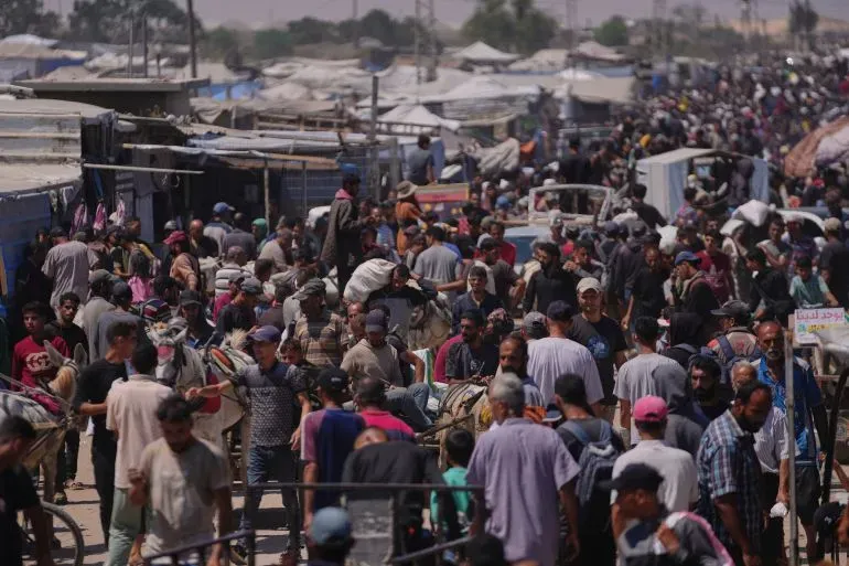 ازدحام كبير في منطقة تضم العديد من الفلسطينيين النازحين في رفح، مع وجود خيام ومركبات في الخلفية، يعكس الوضع الإنساني المتدهور.