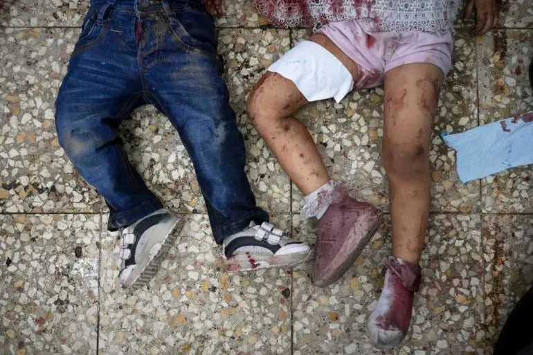 جثتا طفلين ملطختين بالدماء على أرضية مغطاة بالبلاط، تعكسان الأثر المدمر للصراع في غزة.