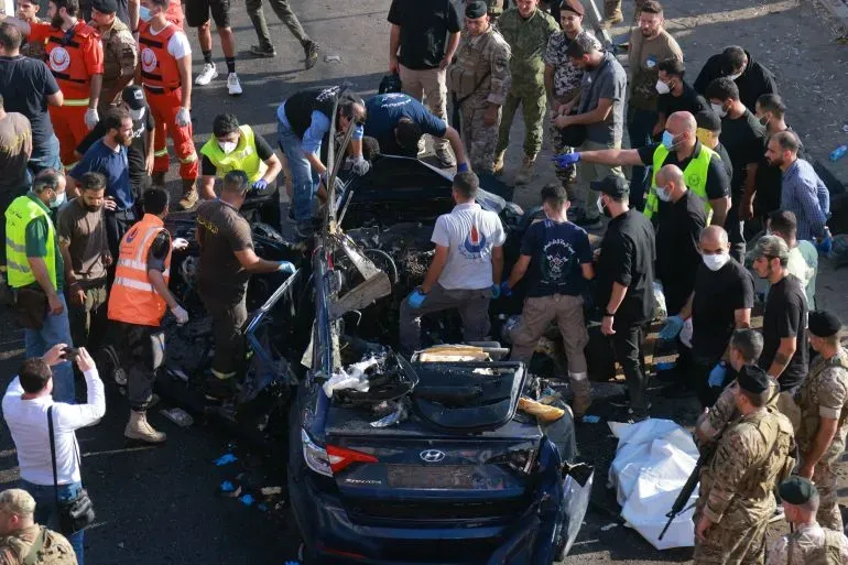 موقع الحادث في بلدة شقرا بعد غارة إسرائيلية، حيث يتجمع رجال الإنقاذ والجنود حول سيارة مدمرة، مع وجود مصابين في الموقع.