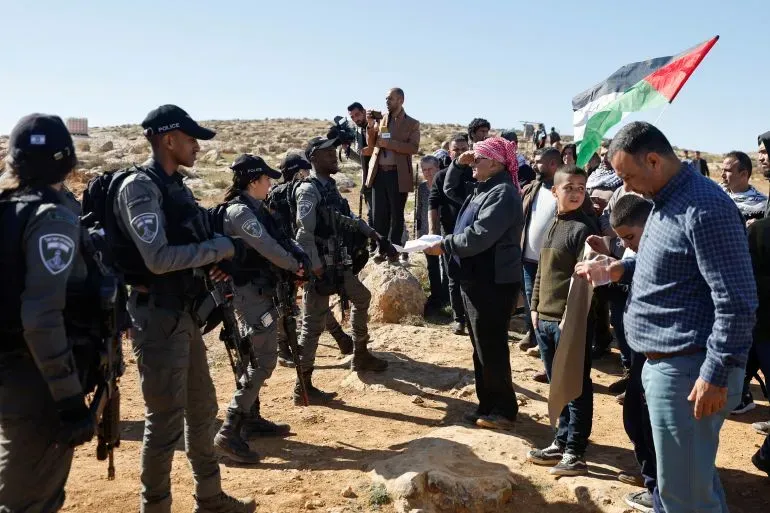 مظاهرة في قرية أم الخير بالضفة الغربية، حيث يتواجد جنود إسرائيليون ومواطنون فلسطينيون يتحدثون معاً وسط توتر سياسي.