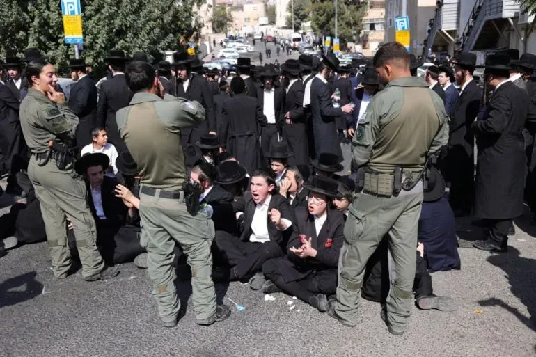 تجمع حشود من رجال الدين اليهود المتشددين في الشارع، بينما تراقبهم قوات الأمن، في سياق احتجاجات ضد قانون الخدمة العسكرية.