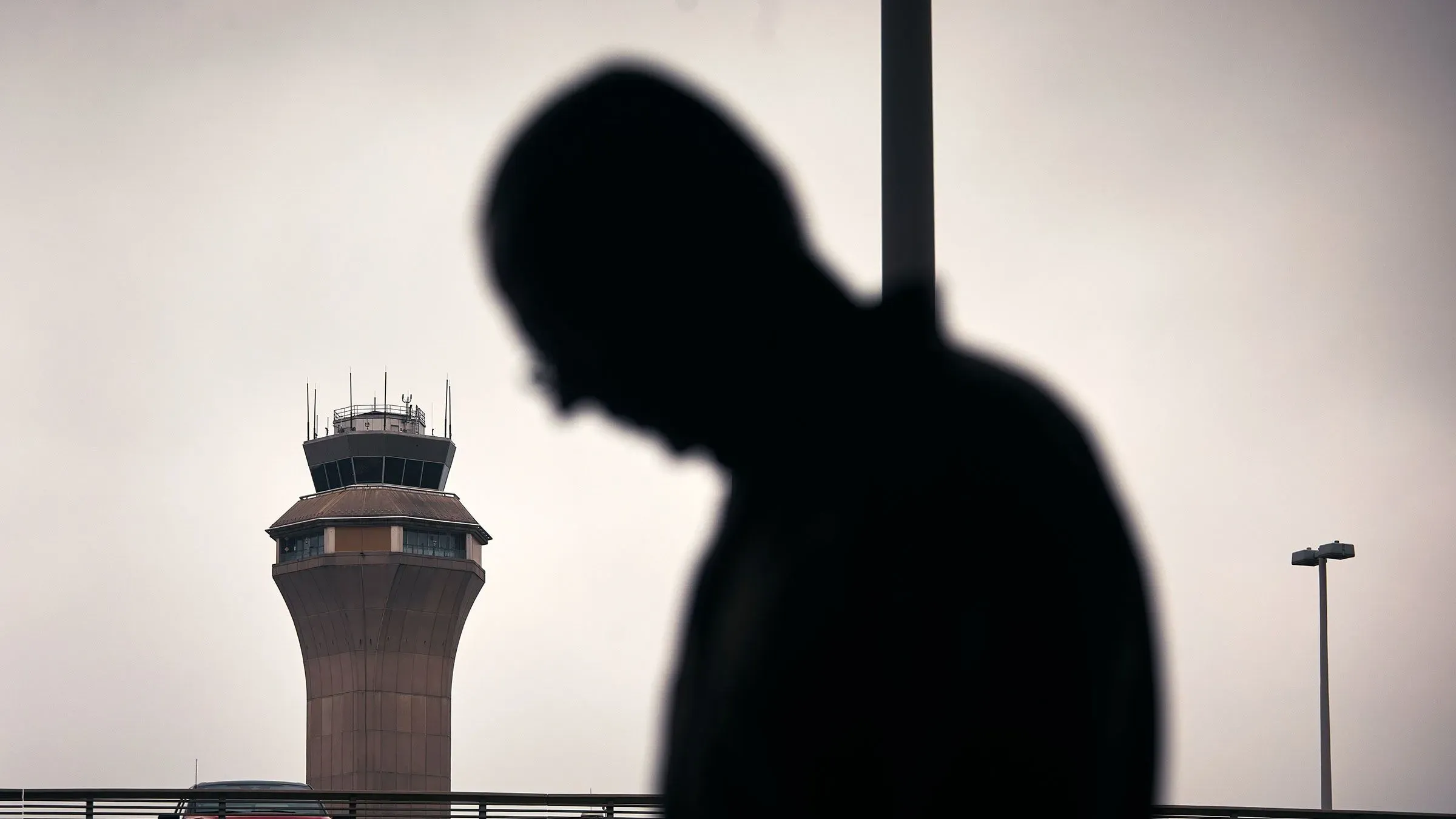 ظل شخص يقف أمام برج مراقبة مطار نيوارك ليبرتي الدولي، مع أجواء غائمة تعكس التحديات التي يواجهها المطار.