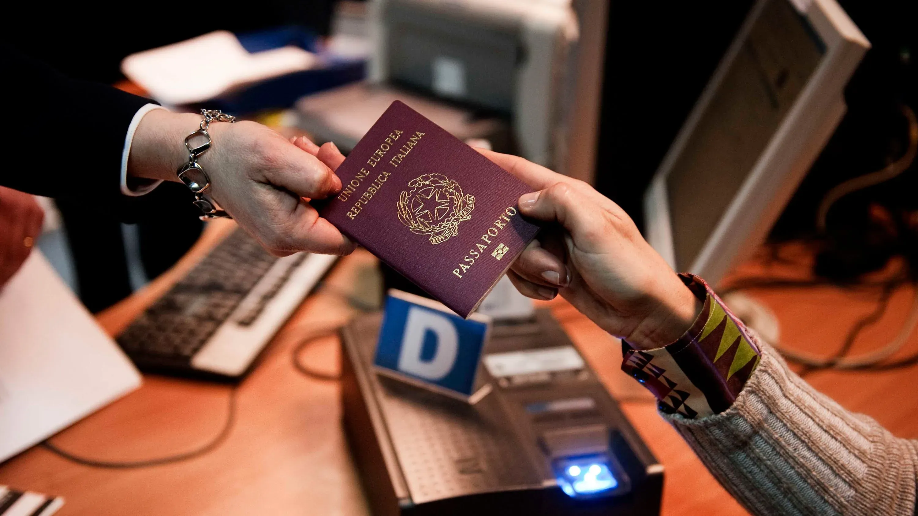 جواز سفر إيطالي يُسلم من موظف في قنصلية، مما يعكس التحديات المتعلقة بالحصول على الجنسية الإيطالية للمولودين في الخارج.