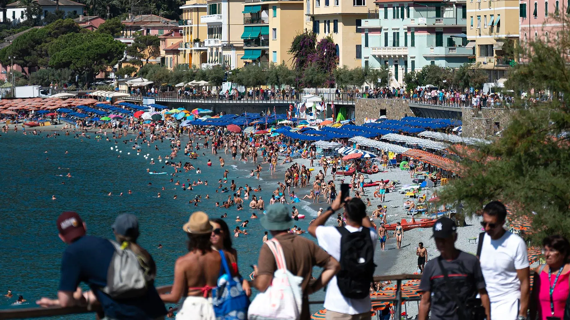 شاطئ مزدحم في إيطاليا مع أشخاص يستمتعون بأشعة الشمس، وأكواخ ملونة ومظلات، مما يعكس جاذبية السياحة الإيطالية.