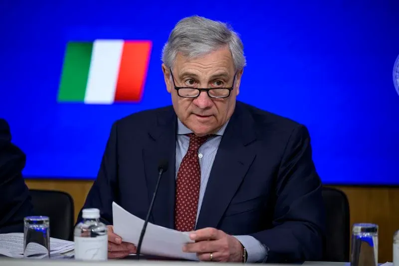 وزير الخارجية الإيطالي أنطونيو تاجاني يتحدث في مؤتمر صحفي، مع العلم الإيطالي في الخلفية، حول تغييرات قوانين الجنسية.