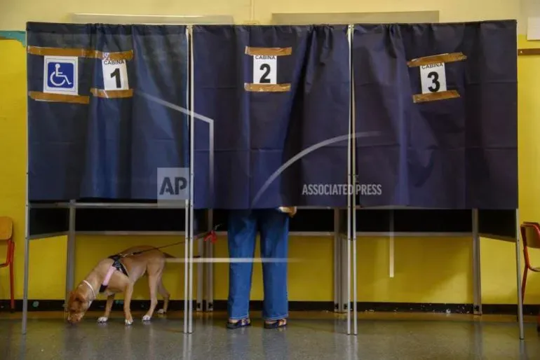 مركز اقتراع في إيطاليا مع ستائر تفصل بين صناديق الاقتراع، وشخص يقف خلف أحدها مع كلبه، في سياق استفتاء حول الجنسية.