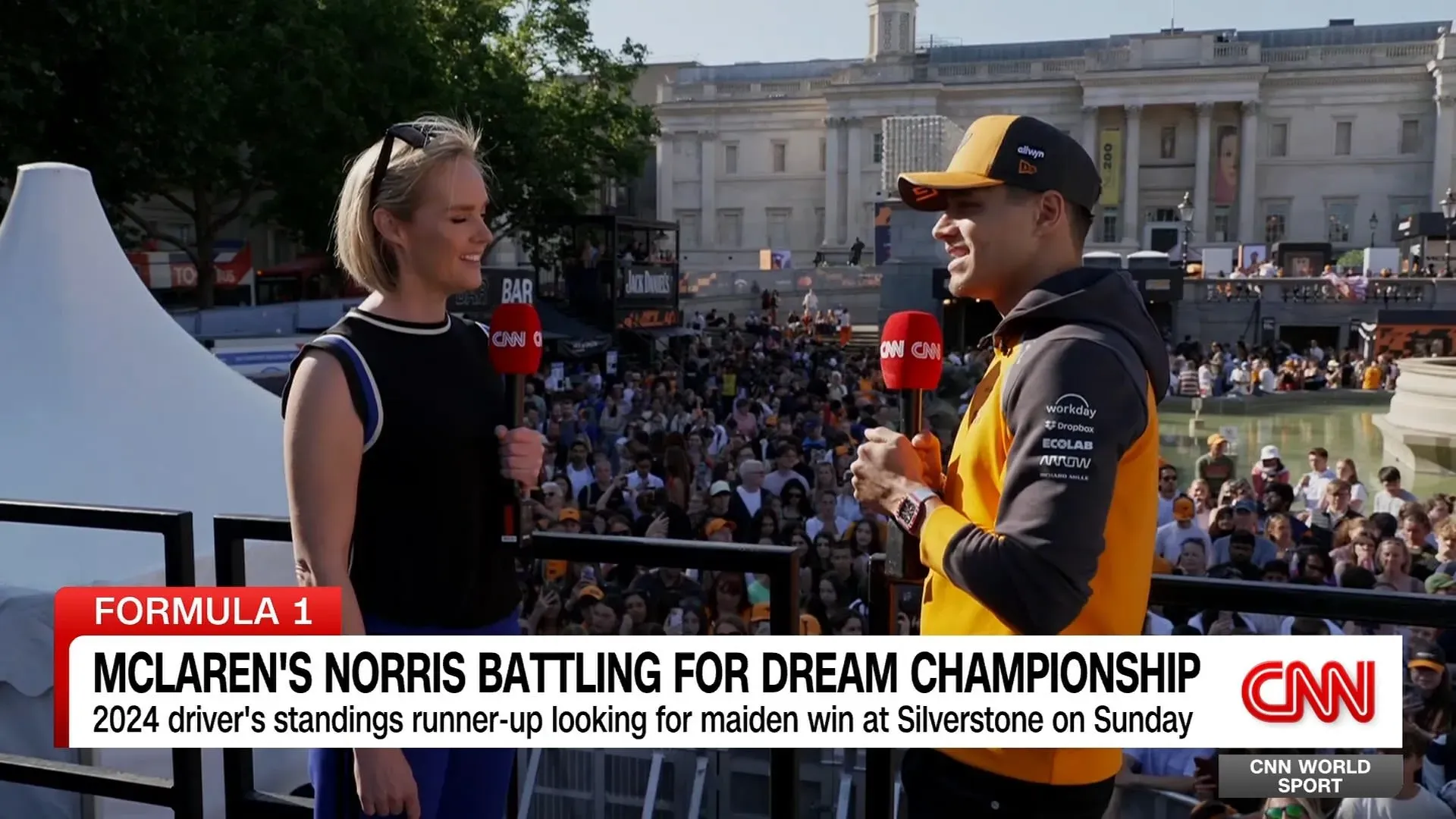 لاندو نوريس يتحدث مع مراسلة CNN وسط حشد كبير من المشجعين في ساحة ترافالغار، مستعداً للسباق في سيلفرستون.
