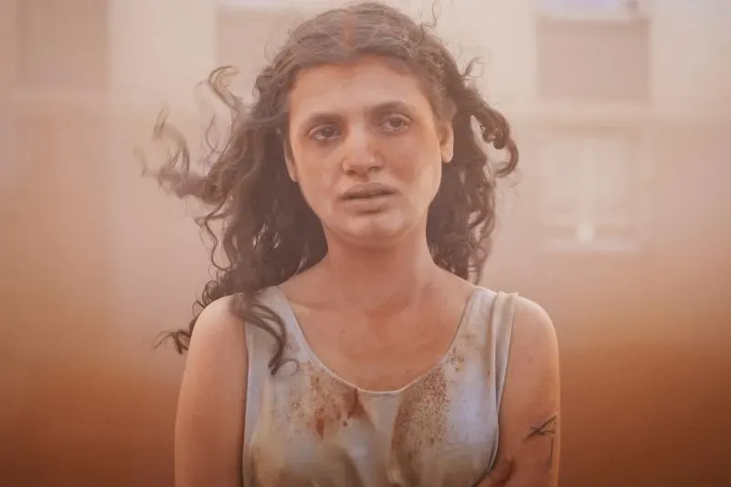 امرأة ذات شعر مجعد وملابس متسخة، تبدو في حالة قلق وسط بيئة صحراوية، تعكس مشاعر الاضطراب والفوضى في مهرجان كان السينمائي.