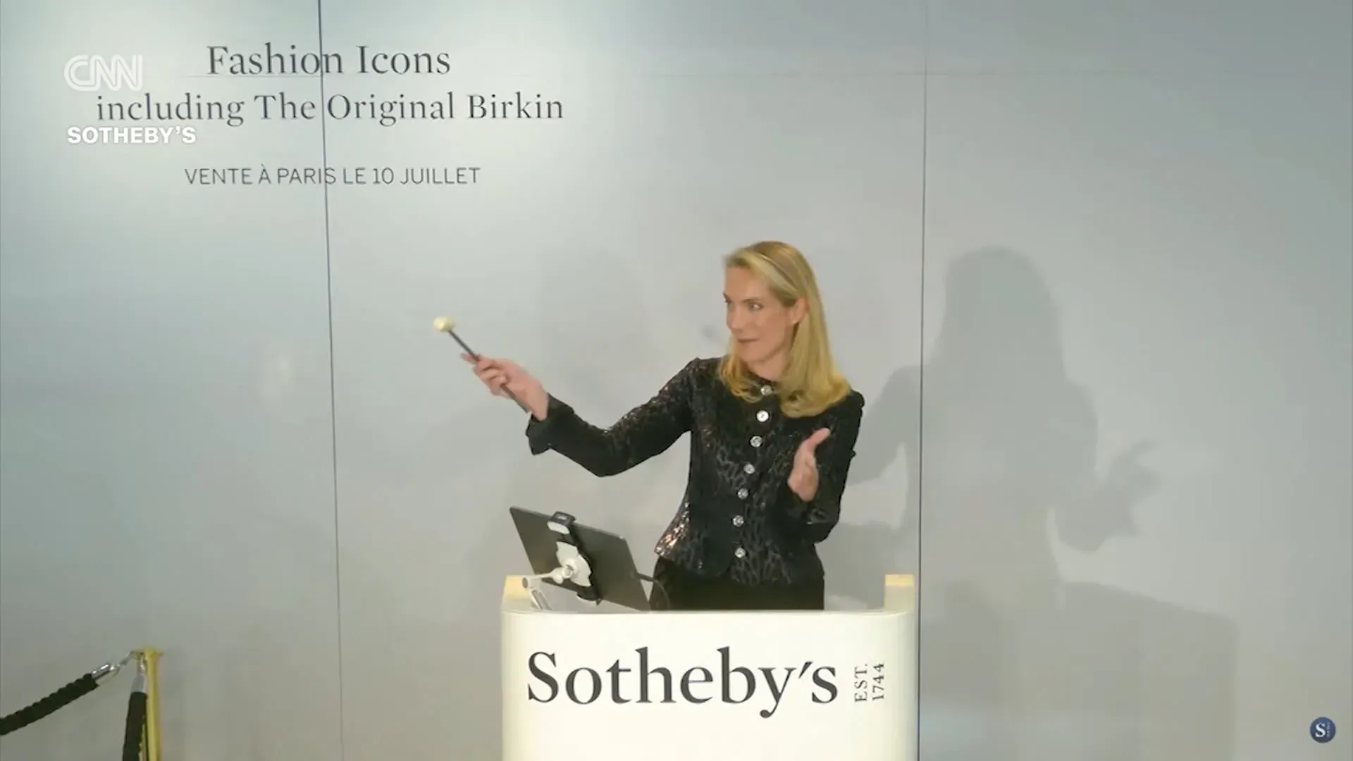 امرأة ترتدي سترة أنيقة تشير بعصا المزاد خلال مزاد حقيبة بيركين الأصلية في دار سوذبيز، باريس، في 10 يوليو.