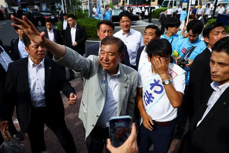 مجموعة من السياسيين اليابانيين في تجمع انتخابي، مع أحدهم يلوح بيده، بينما يظهر آخر يبدو عليه القلق.