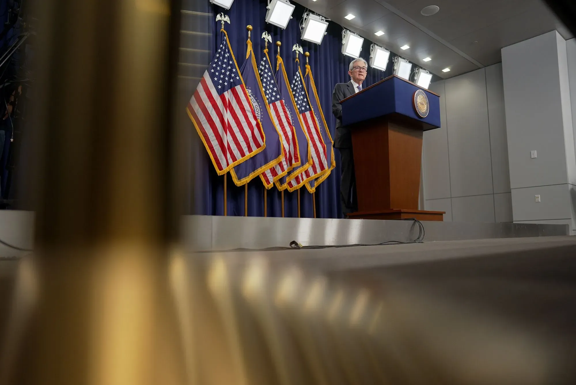 جيروم باول يتحدث في مؤتمر صحفي، مع أعلام الولايات المتحدة خلفه، مع التركيز على أهمية استقلال الاحتياطي الفيدرالي.