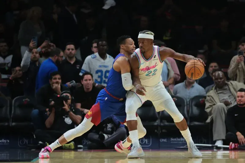 جيمي بتلر خلال مباراة أمام دنفر ناجتس، محاولاً التهرب من دفاع اللاعب المنافس، وسط جمهور مشجع.