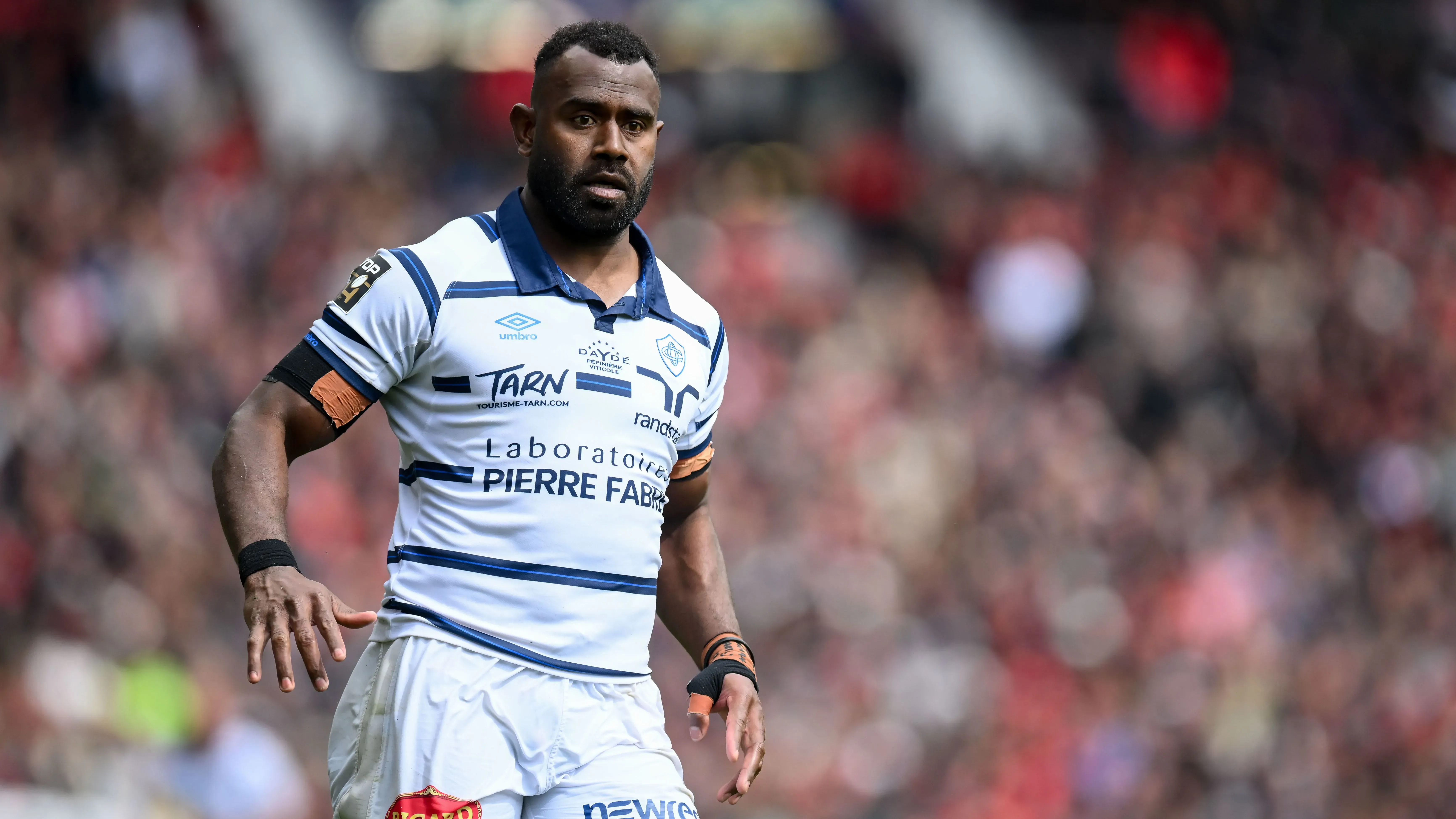 تظهر الصورة لاعب الرجبي جوسيا رايسوكي أثناء مباراة، مرتديًا زي نادي كاستريس أولمبيك، مع خلفية جماهيرية.