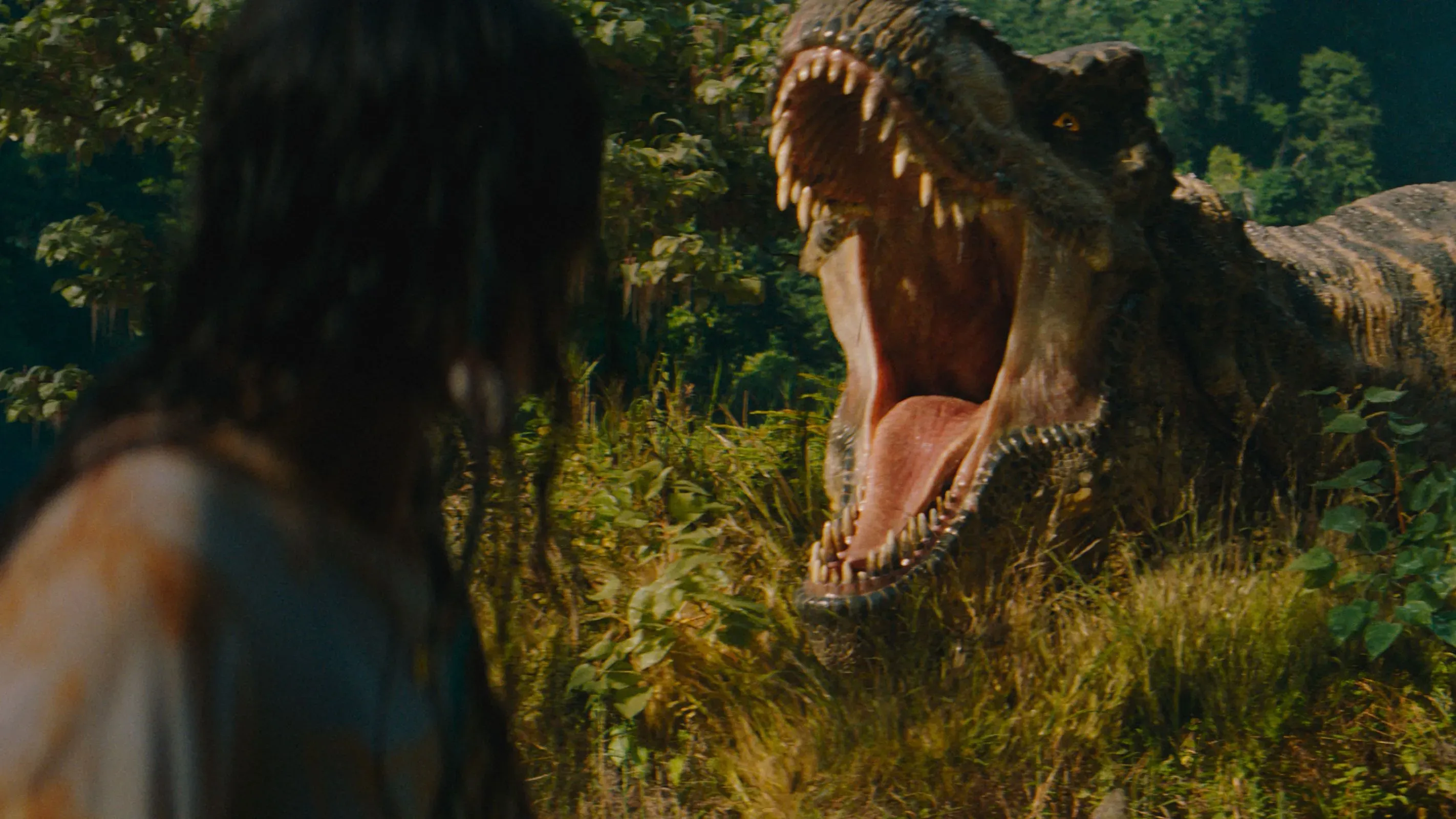 ديناصور تي-rex يفتح فمه في مشهد مثير من فيلم "Jurassic World Rebirth"، مع خلفية طبيعية خضراء وشخصية بشرية في المقدمة.