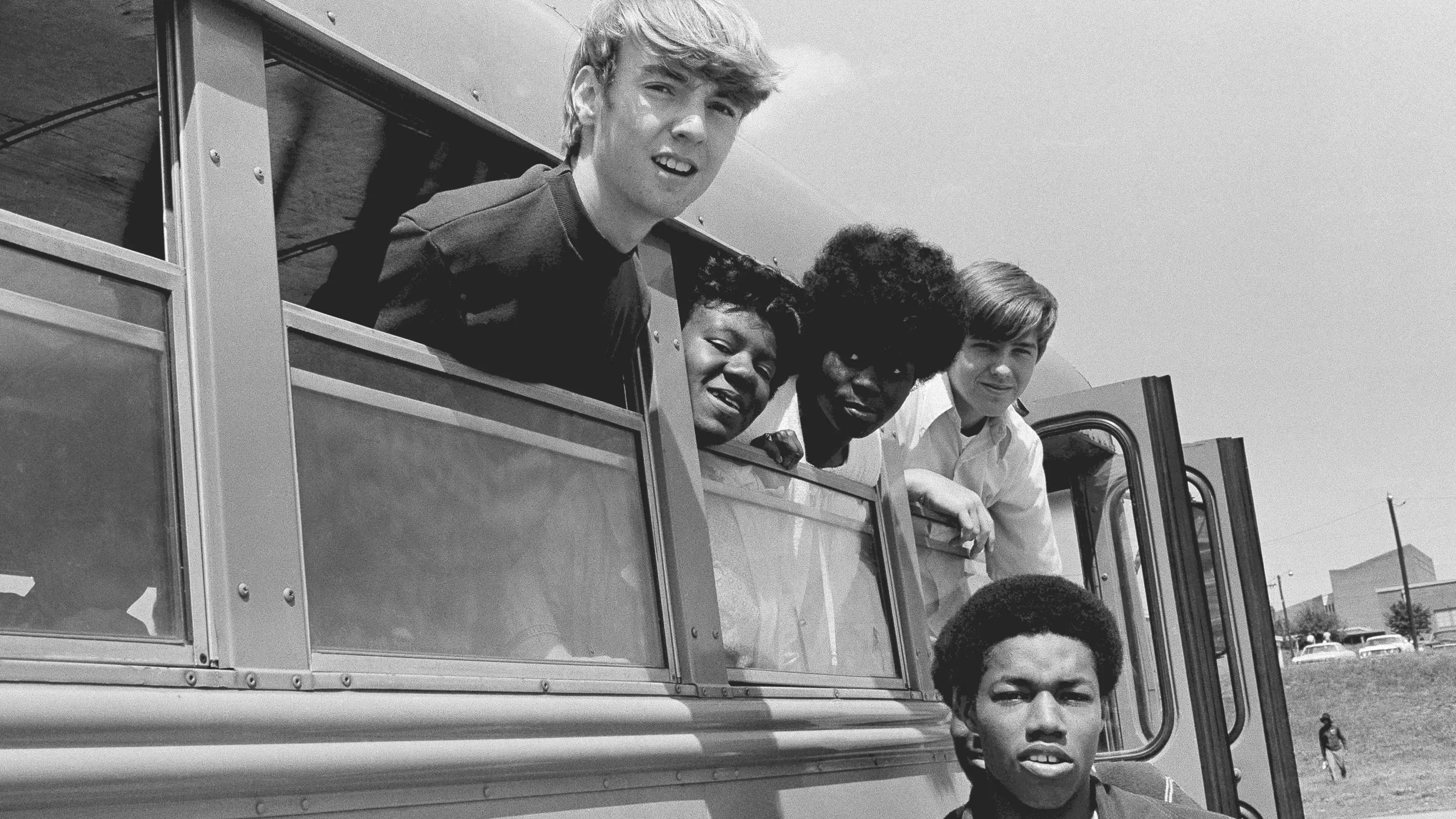 مجموعة من الطلاب من خلف نافذة حافلة مدرسية، يظهرون معًا في لحظة تعبير عن التنوع والاندماج، في سياق إلغاء الفصل العنصري في التعليم.