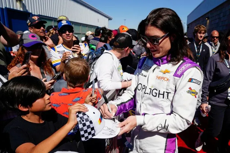 كاثرين ليج، سائقة سباقات بريطانية، توقع توقيعها على قبعة لصبي وسط حشد من المعجبين في حدث سباقات ناسكار، تعبيراً عن دعمها للنساء في رياضة السيارات.