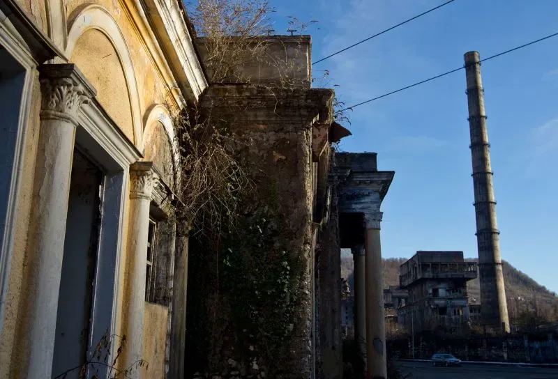 مشهد لمستودع مهجور في سوخومي، أبخازيا، مع عمود مدخنة مرتفع، يرمز إلى تأثير تعدين العملات الرقمية على المنطقة.