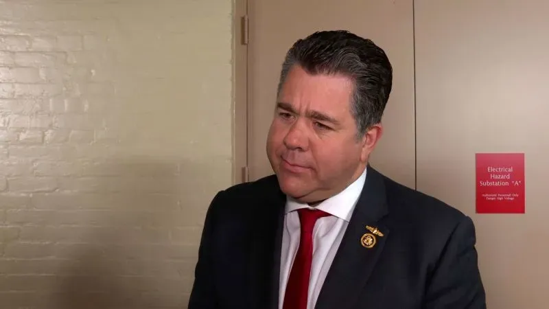 النائب مايك جونسون يتحدث في ممر مجلس النواب، مع وجود لافتة تحذيرية خلفه. يواجه ضغوطاً من فصائل الحزب الجمهوري المختلفة حول مشروع قانون الميزانية.