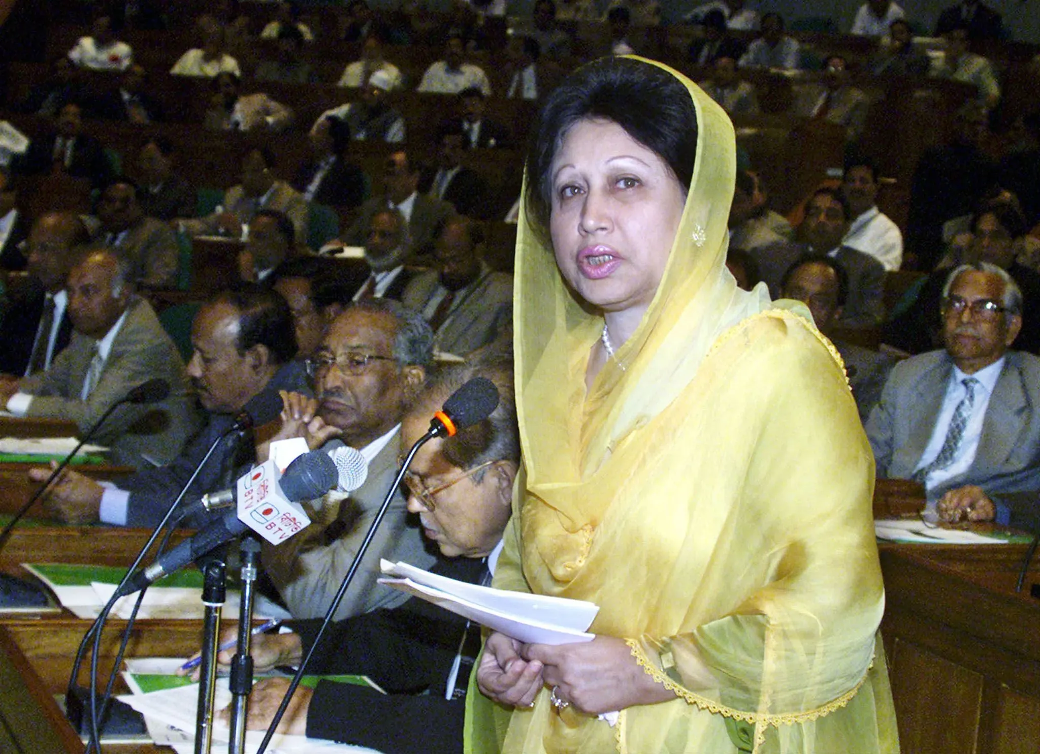رئيسة وزراء بنغلاديش السابقة خالدة ضياء تتحدث في البرلمان، محاطة بأعضاء آخرين، في لحظة تاريخية تعكس تأثيرها السياسي.