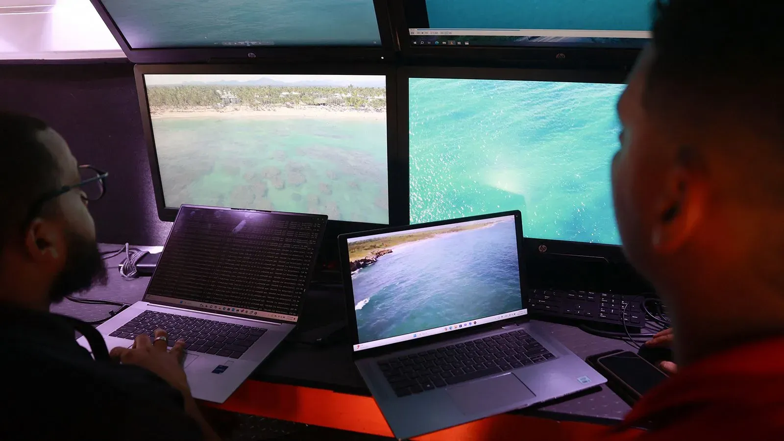 موظفان يراقبان شاشات متعددة أثناء البحث عن الطالبة المفقودة سوديكشا كونانكي، مع عرض لقطات من الساحل والمياه.