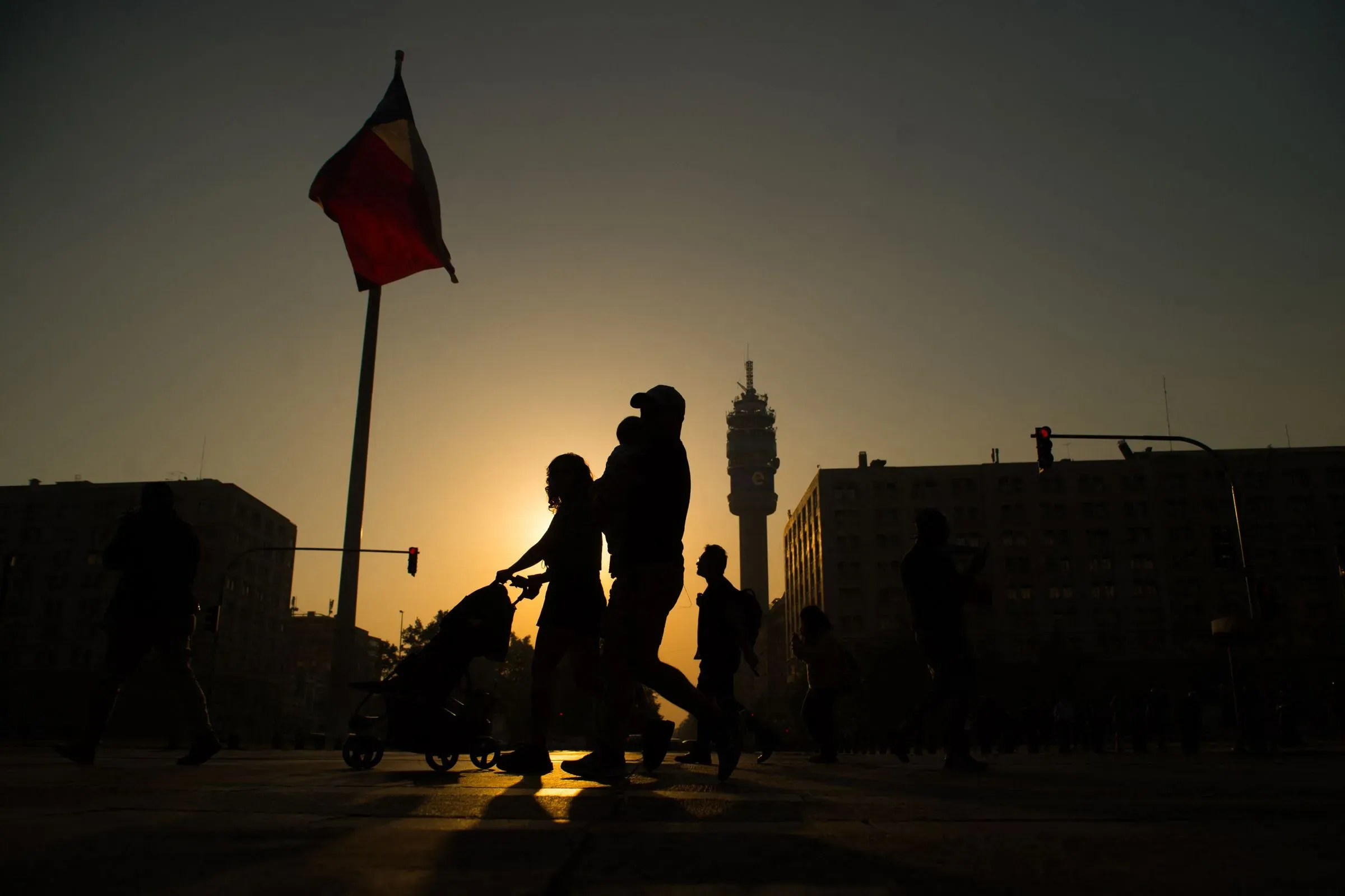 مشهد يظهر silhouettes لأشخاص يسيرون في شارع فيسبوسيو سور في سانتياغو، مع علم تشيلي يرفرف في الخلفية، مما يعكس الحياة الحضرية المتنوعة.