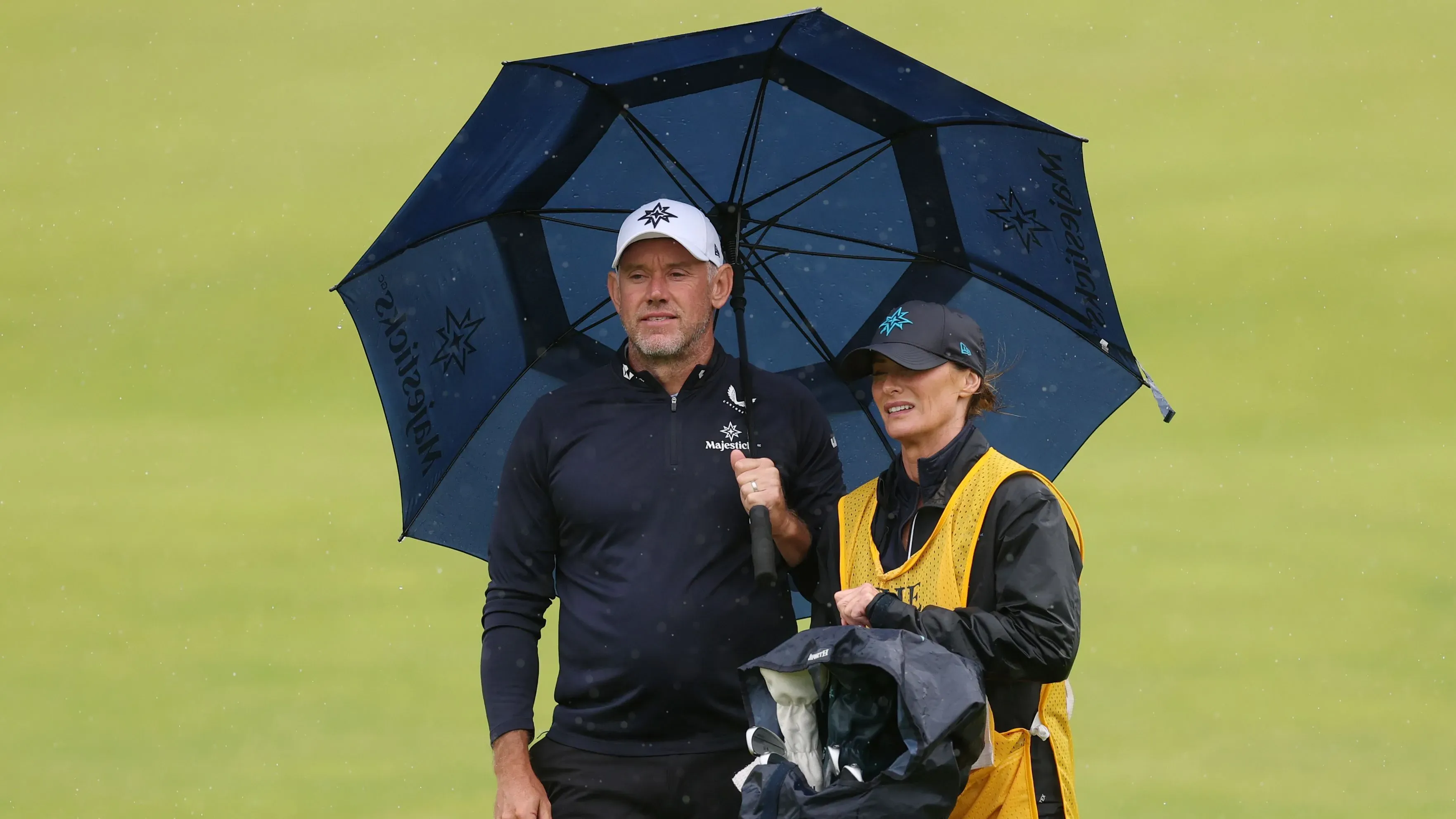 لي ويستوود وزوجته هيلين تحت مظلة في يوم ممطر خلال بطولة الجولف المفتوحة، حيث تقود هيلين الجولة كحاملة حقيبة.