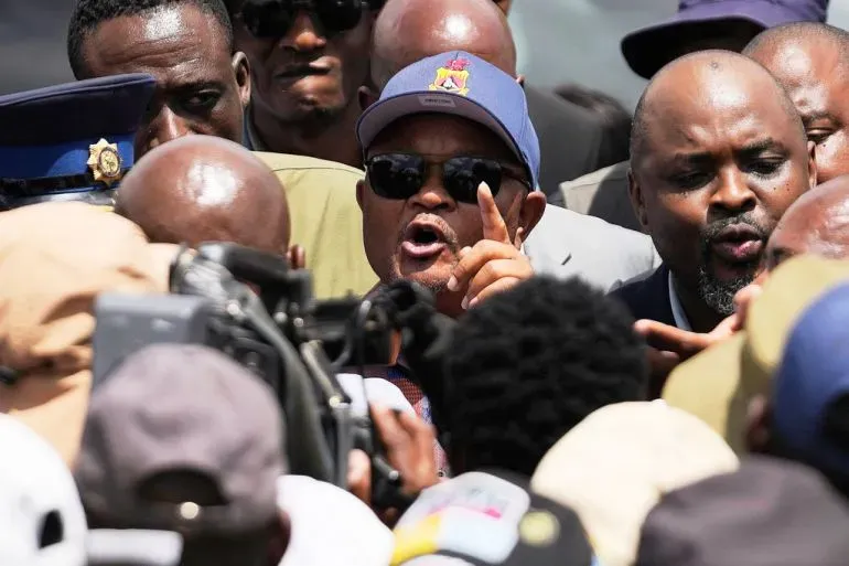 مخاوانازي يتحدث بحماس أثناء مؤتمر صحفي، محاطًا بجمهور من الصحفيين والمناصرين، مع التركيز على قضايا الفساد في جنوب أفريقيا.