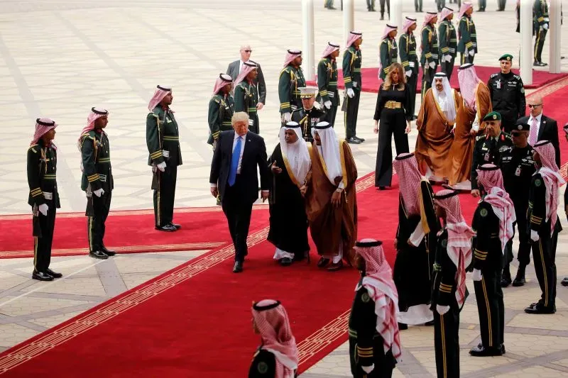 دونالد ترامب يتجول مع مسؤولين سعوديين في استقبال رسمي، وسط حراس يرتدون زيًا عسكريًا، على سجادة حمراء في زيارة للشرق الأوسط.