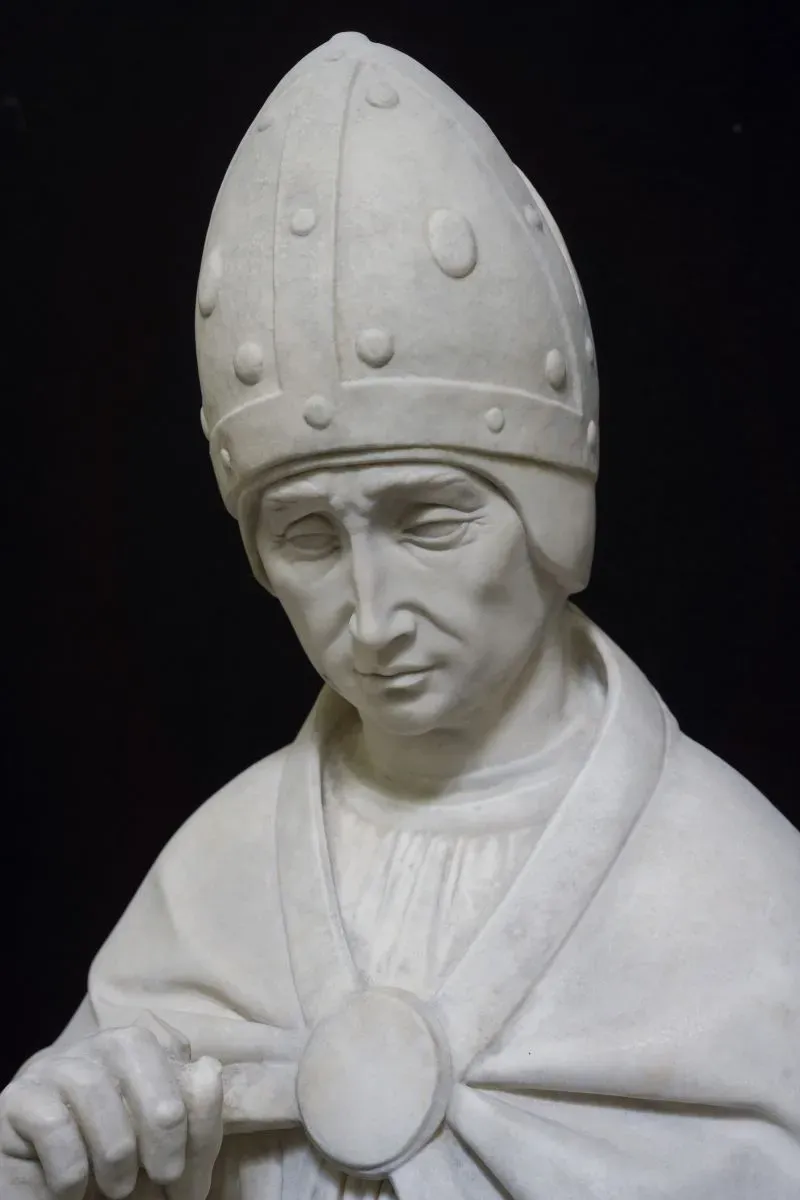 تمثال نصفي من الرخام لشخصية دينية، يظهر بتفاصيل دقيقة مثل القبعة والتعابير العاطفية، يعكس أسلوب مايكل أنجلو في النحت.
