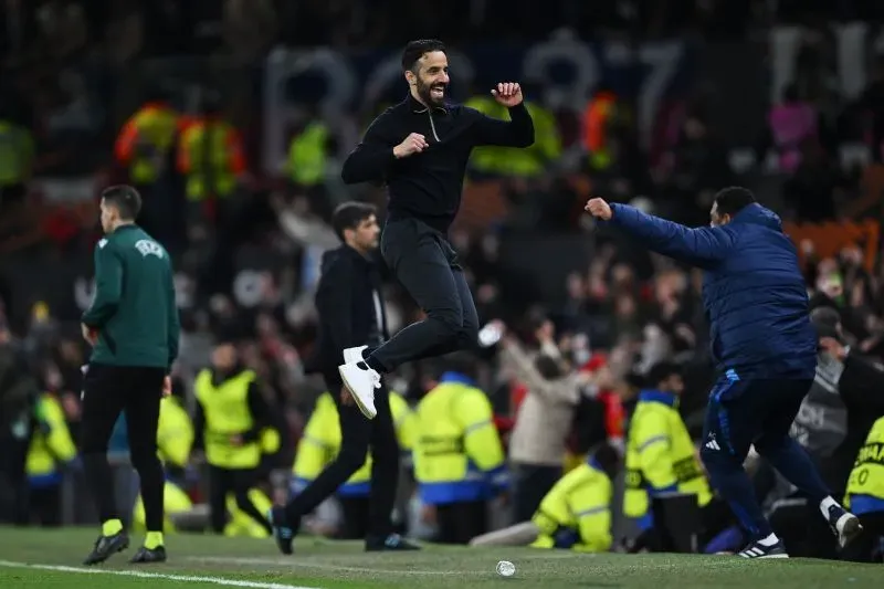 مدرب يونايتد يحتفل بفوز فريقه المفاجئ في مباراة دوري أبطال أوروبا، مع مشجعين متحمسين في الخلفية.