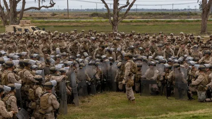 تجمع كبير لقوات مشاة البحرية الأمريكية في موقع مفتوح، حيث يقف الضباط في صفوف مع دروع، استعدادًا لدعم عمليات إنفاذ القانون في لوس أنجلوس.