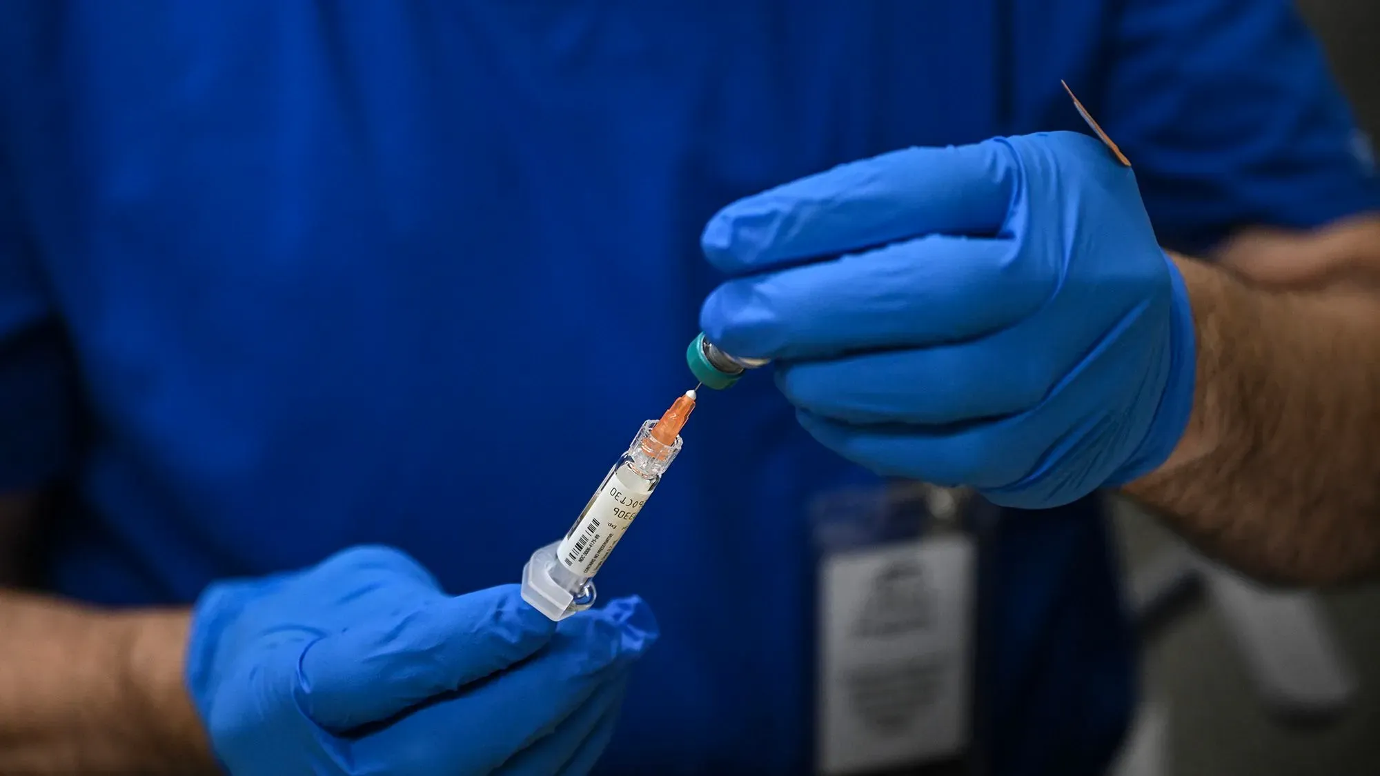 حقنة لقاح الحصبة في يد ممارس صحي يرتدي قفازات زرقاء، تعكس جهود التطعيم لمواجهة تفشي الحصبة في تكساس ونيو مكسيكو.