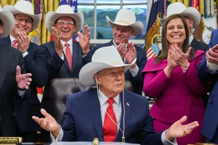 ترامب يجلس في المكتب البيضاوي مرتديًا قبعة رعاة البقر، محاطًا بمؤيدين يصفقون له، مما يعكس أجواء سياسية متوترة.