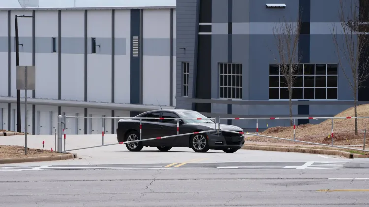 مركبة سوداء متوقفة أمام مستودع كبير، حيث يُخطط لتحويله إلى مركز احتجاز للمهاجرين، مما يثير قلق المجتمع المحلي.