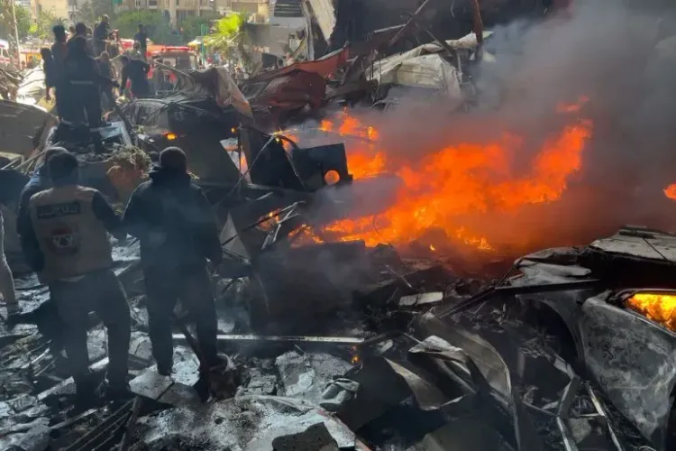 دخان يتصاعد من حطام مبنى بعد هجوم إسرائيلي في لبنان، حيث يتجمع رجال الإنقاذ وسط الفوضى. الهجوم أسفر عن مقتل وإصابة العشرات.