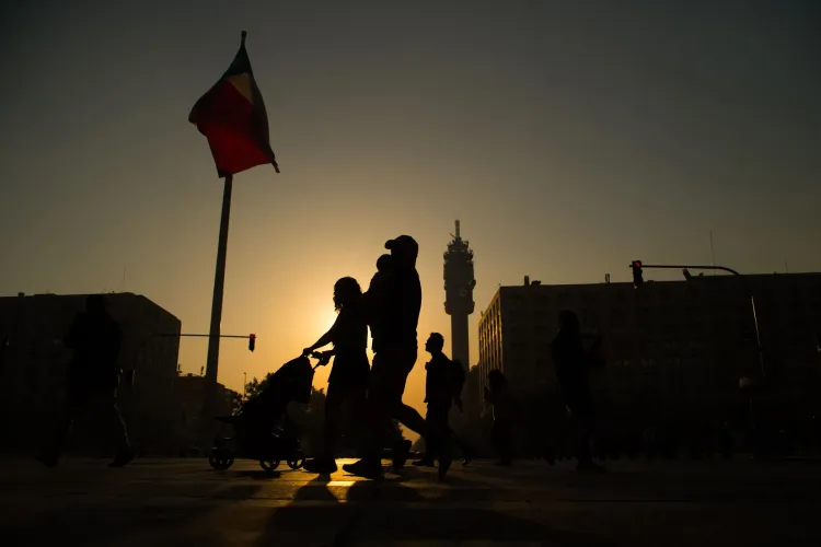 مشهد يظهر silhouettes لأشخاص يسيرون في شارع فيسبوسيو سور في سانتياغو، مع علم تشيلي يرفرف في الخلفية، مما يعكس الحياة الحضرية المتنوعة.