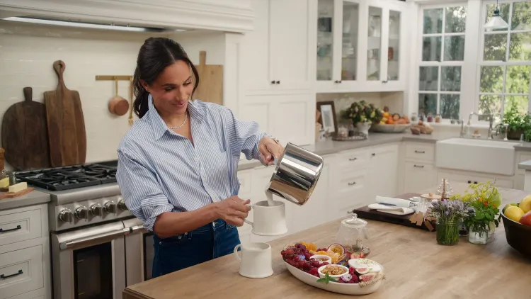 ميغان ماركل تصب الشاي في مطبخ أنيق، محاطة بأدوات منزلية من علامتها التجارية "As Ever"، تعكس أسلوب حياتها المميز.