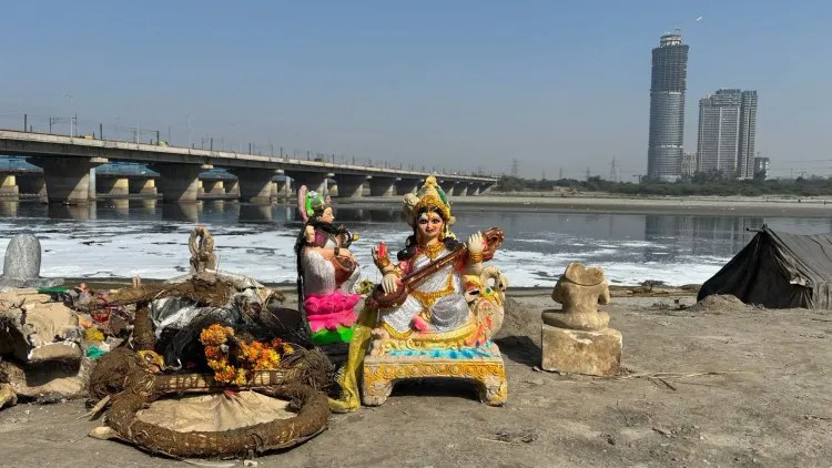 تمثال لآلهة هندوسية محاط بالنفايات على ضفاف نهر يامونا الملوث، مع خلفية تظهر جسرًا ومبانٍ حديثة في دلهي.