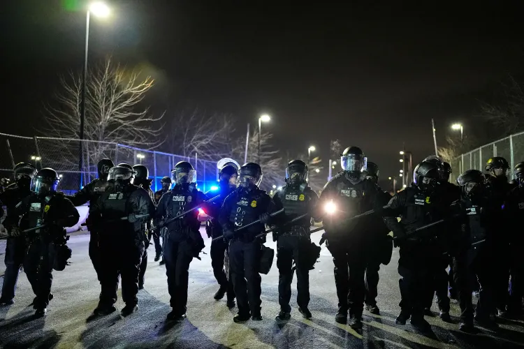 عناصر مسلحة من وكالة إنفاذ قوانين الهجرة والجمارك في مينيابوليس، يرتدون دروعًا ويستعدون لمواجهة المحتجين في أجواء مشحونة.