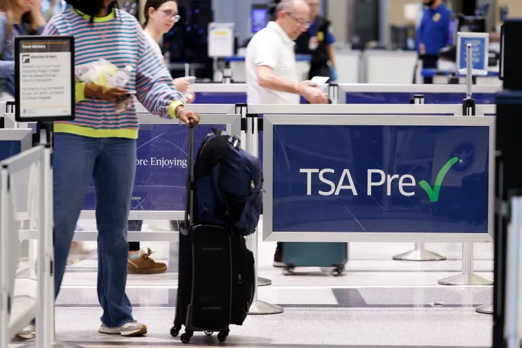 ازدحام في مطار مع وجود لافتة تشير إلى "TSA Pre" بينما يسير مسافرون يحملون حقائبهم، مما يعكس تأثير الإغلاق الجزئي على السفر.