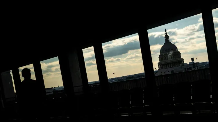 ظل شخص يقف في الظل أمام نوافذ تطل على مبنى الكابيتول الأمريكي، مما يعكس التوترات السياسية في الانتخابات النصفية القادمة.