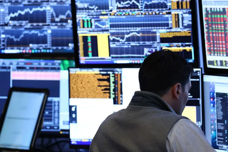 شخص يعمل في غرفة تداول، محاط بشاشات تعرض بيانات سوق الأسهم والرسوم البيانية، مما يعكس تقلبات السوق وأداء الأسهم.