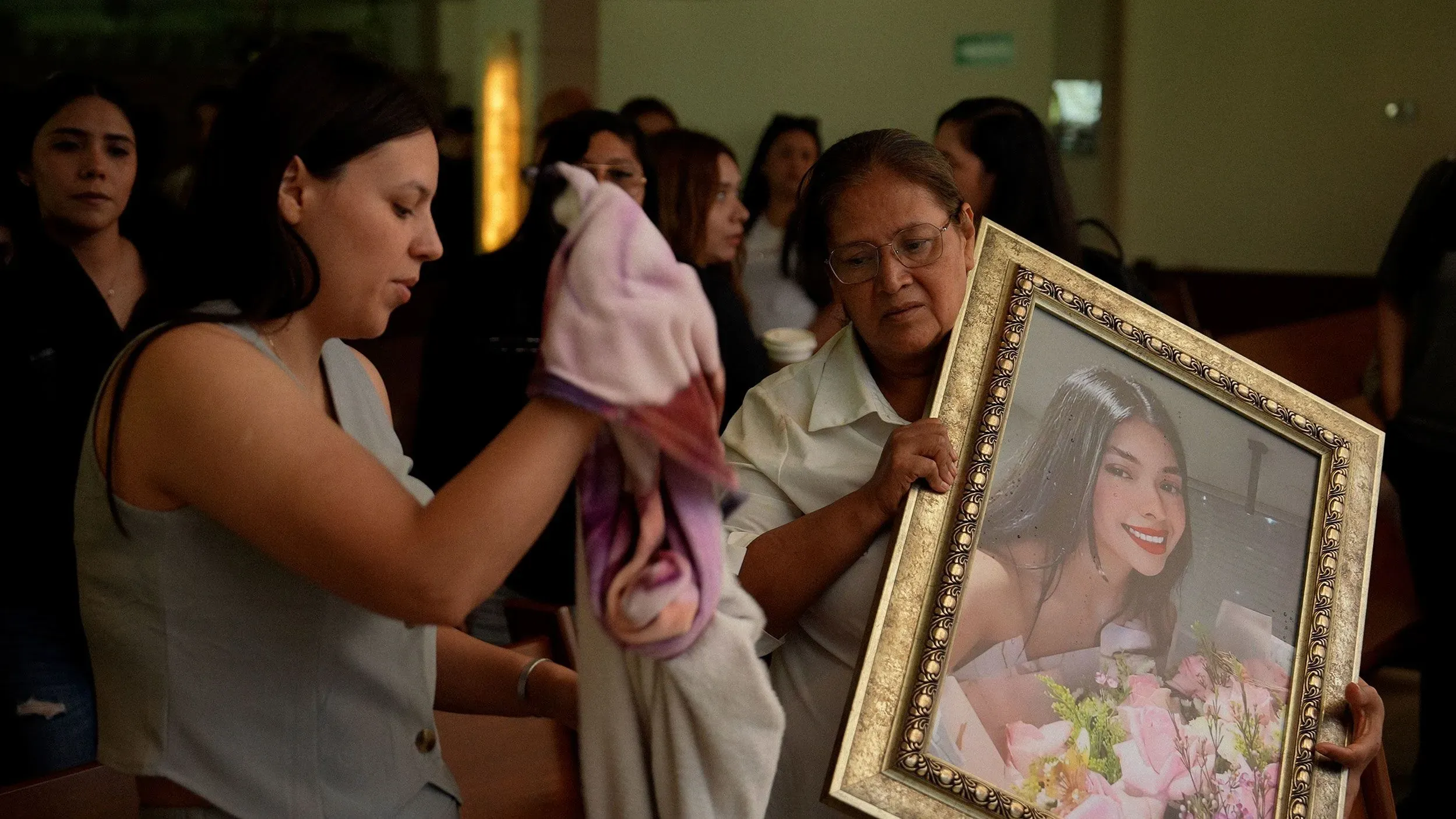 نساء يحملن صورة مؤطرة لفتاة مبتسمة وسط تجمع حزين، يعبرن عن الحزن والفقدان في سياق تأثيرات العنف المرتبط بالعصابات.